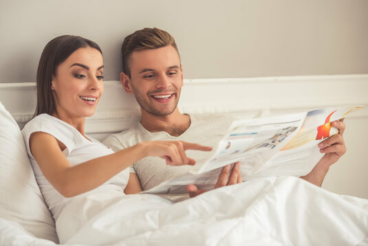 Glückliches Paar liest Zeitung im Bett.