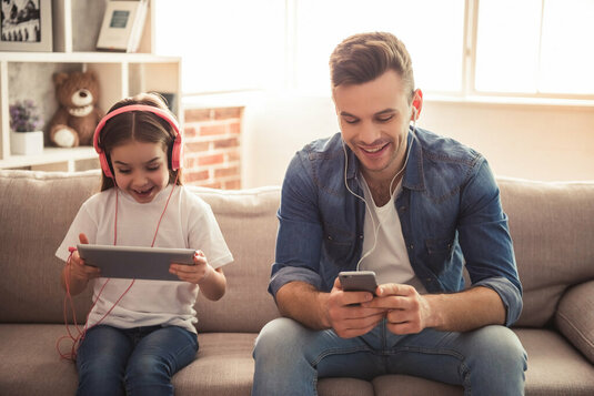 Vater und Tochter sitzen auf der Couch und hören Musik mit Kopfhörern. Vater und Tochter sitzen auf der Couch und hören Musik mit Kopfhörern.